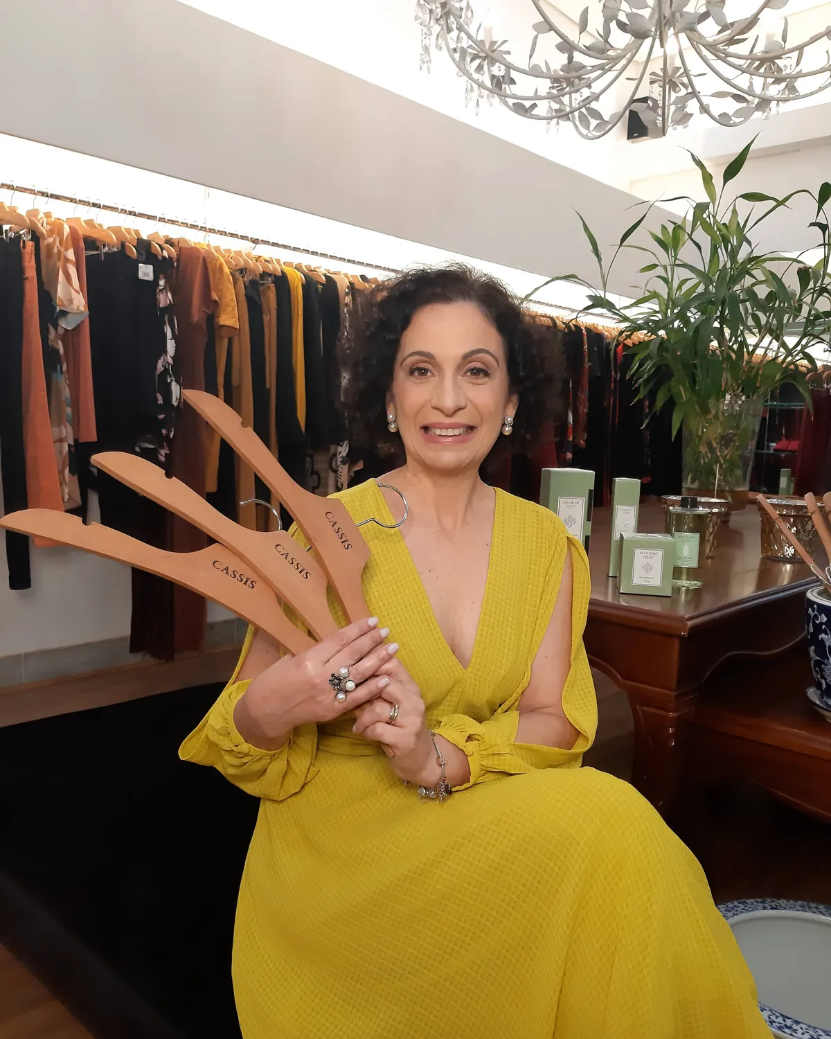 Katia Becegato sorrindo, segurando cabides de madeira em um closet